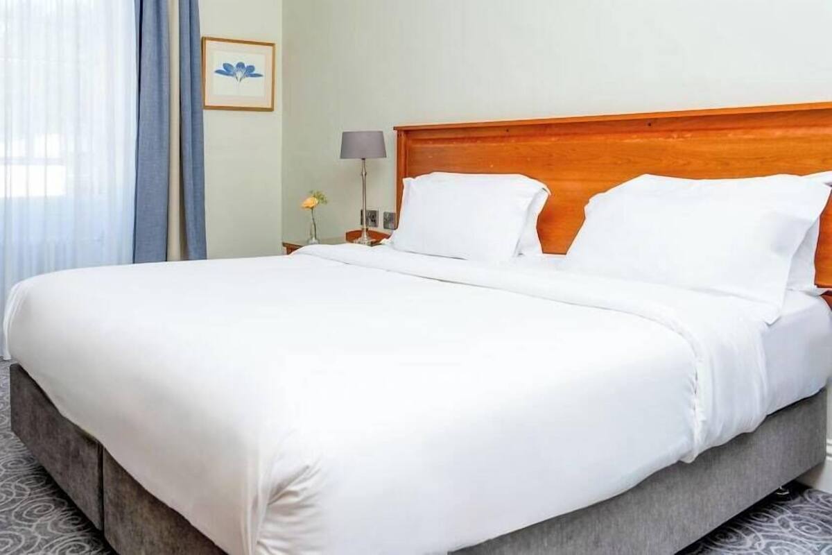 Une chambre d’hôtel avec un grand lit, une tête de lit en bois, une table de chevet avec une lampe et un tableau encadré au mur.