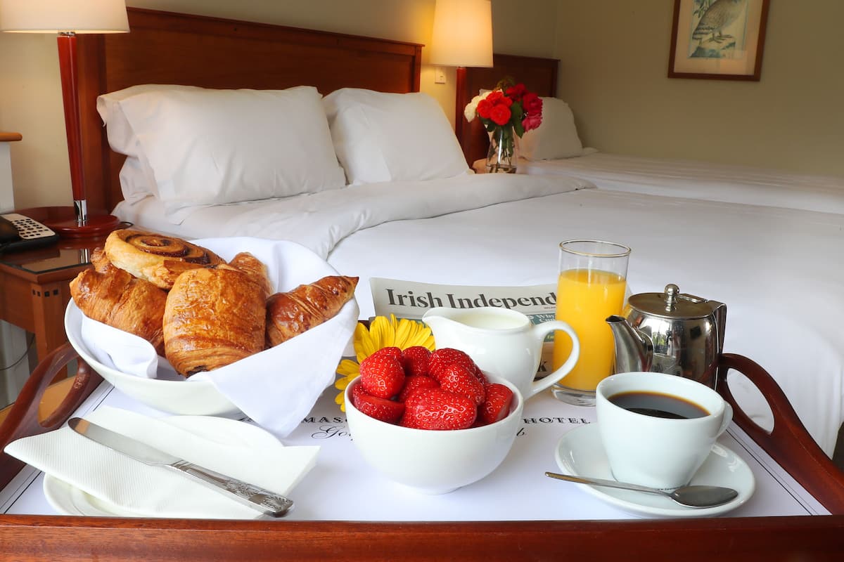 Un plateau de petit-déjeuner bien présenté, avec des croissants, des fraises, une tasse de café et du jus d’orange, posé sur le lit d’un hôtel.