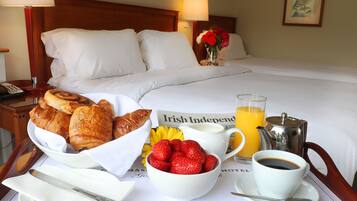 A neatly arranged breakfast tray with croissants, strawberries, a coffee cup, and orange juice on a hotel bed.