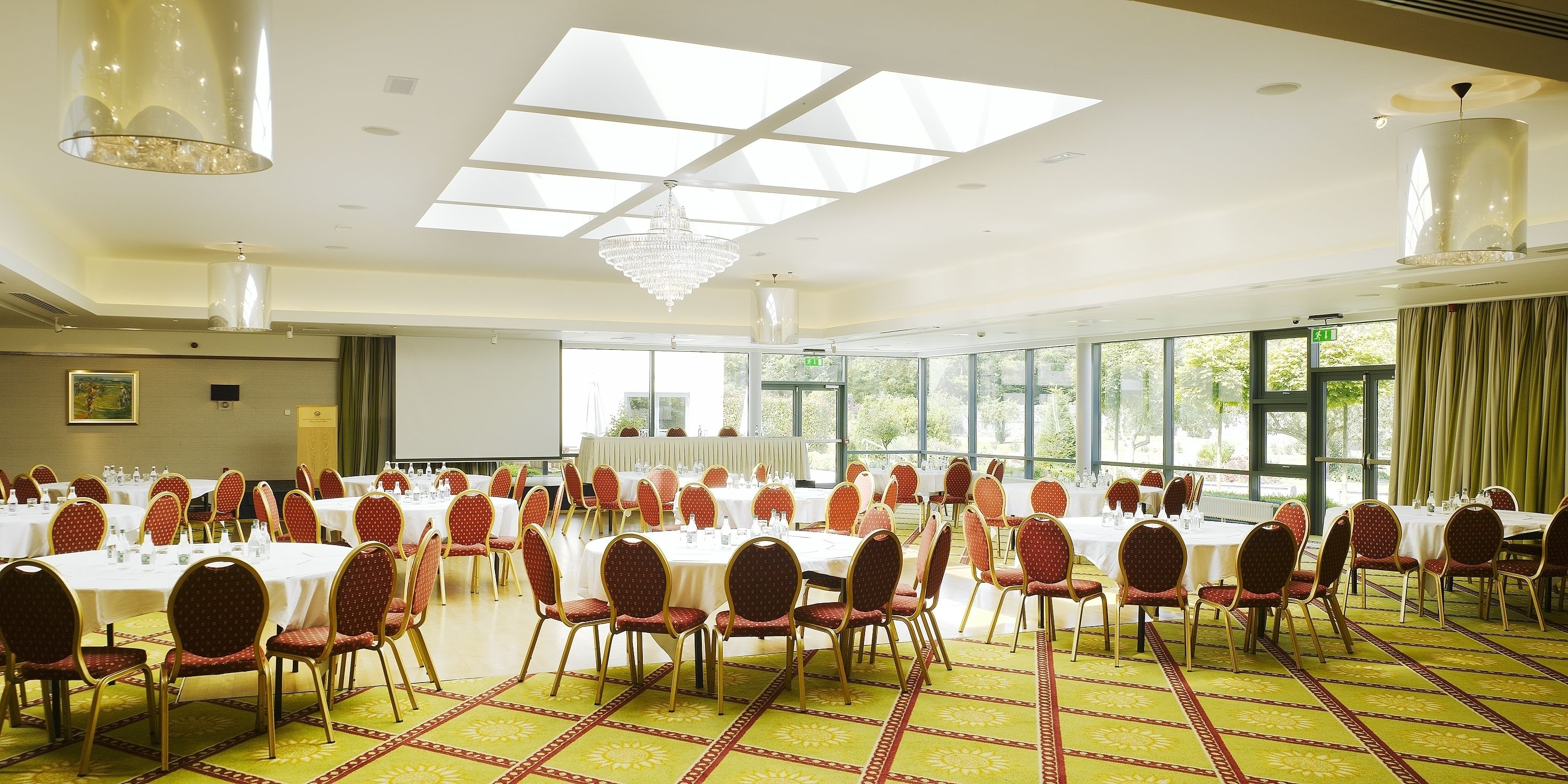 A conference room with round tables and red chairs, large windows, and a chandelier.