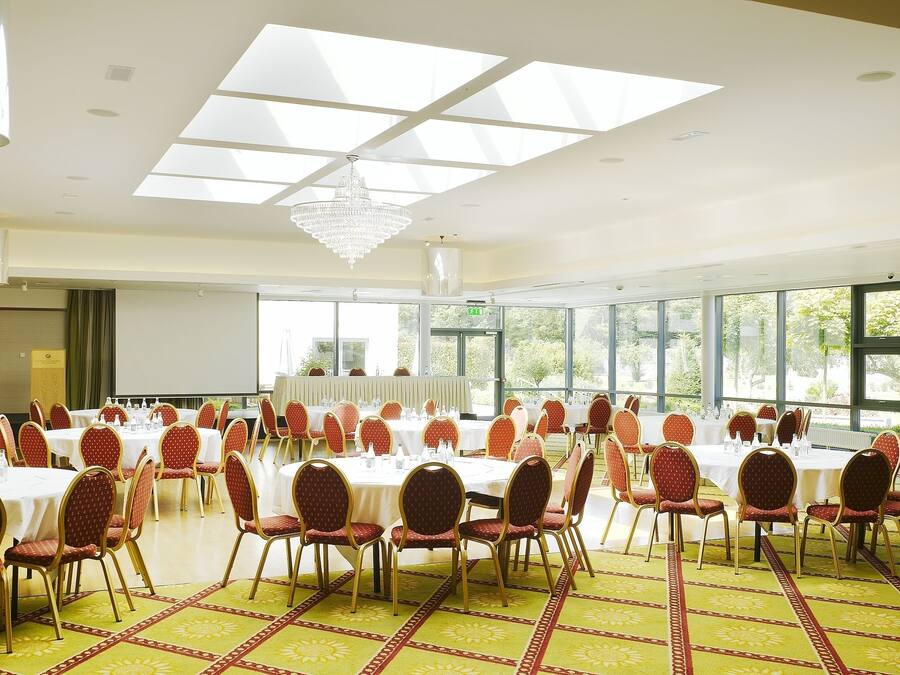 A conference room with round tables and red chairs, large windows, and a chandelier.