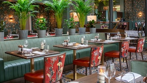 A restaurant with green booths, red floral chairs, and potted plants.