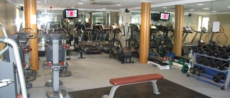 Un gimnasio con cintas de correr, elípticas y pesas libres.