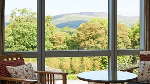 A room with a large window offering a view of green hills and trees.