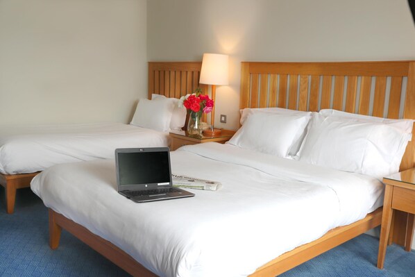A hotel room with two beds, a laptop on the left bed, a lamp on the nightstand, and a vase with flowers.