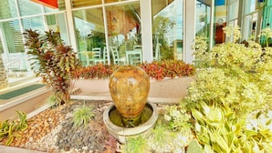 Un jardin d’intérieur bien entretenu, agrémenté d’un grand vase décoratif, de diverses plantes en pot et d’un espace détente avec des chaises.