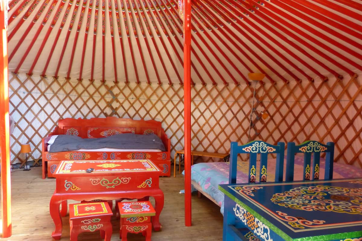 Eine traditionelle Jurte mit einem hölzernen Bett, einem kleinen Tisch und passenden Hockern.