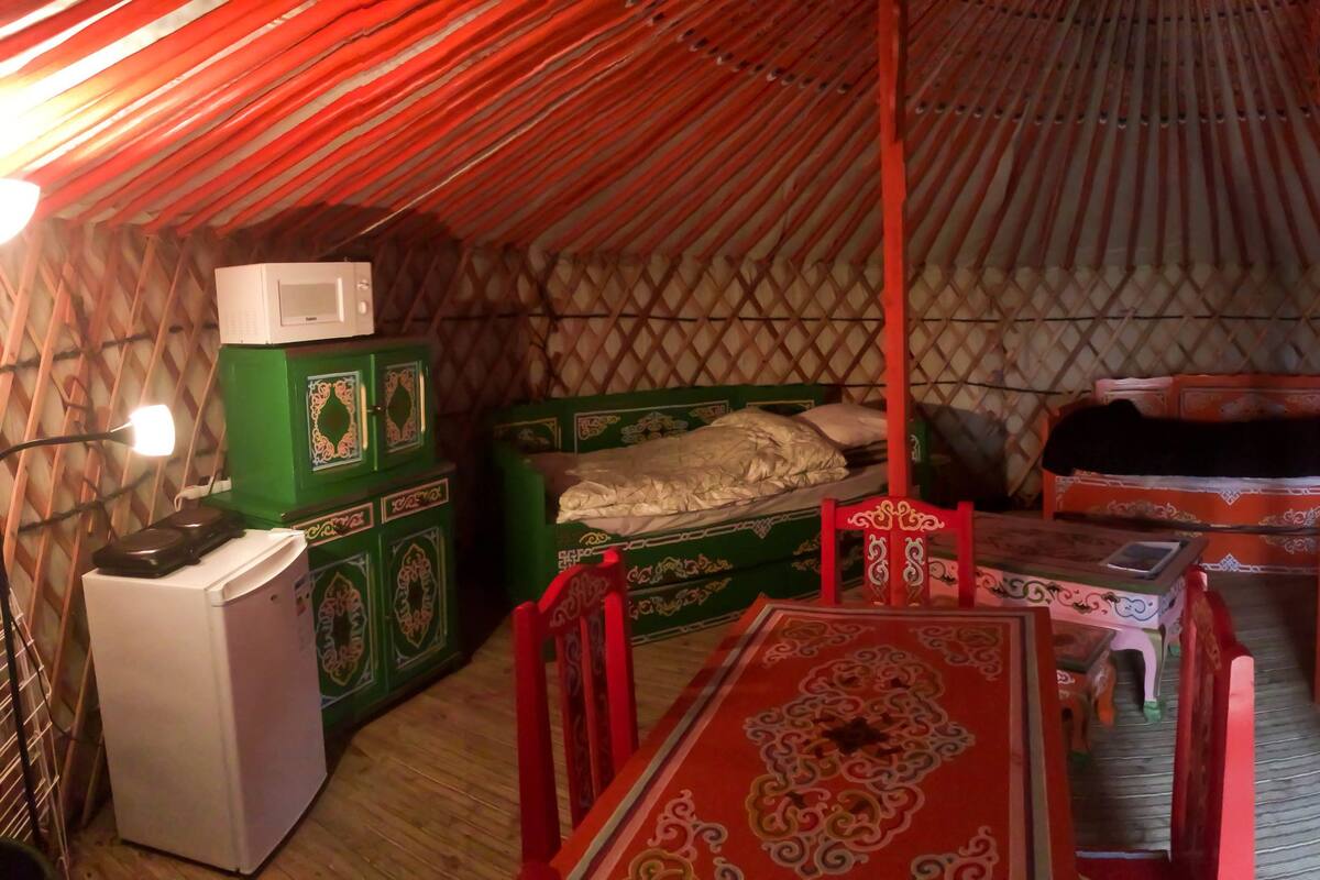 Eine traditionelle Jurte mit einem Bett, einem kleinen Tisch, einem grünen Schrank und einem weißen Gerät.