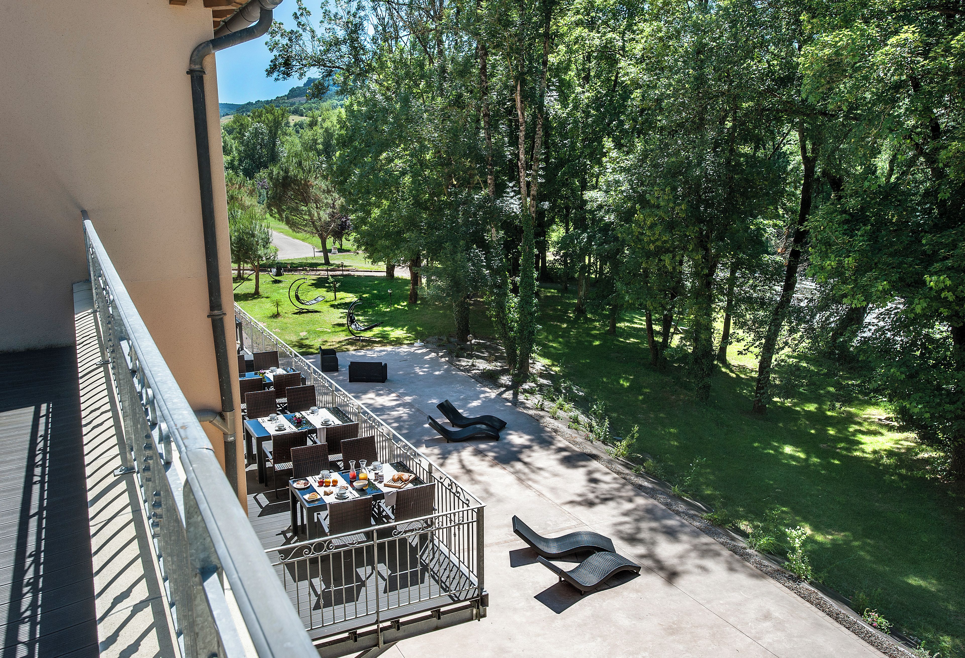 An outdoor terrace with tables and chairs, surrounded by lush greenery and trees.