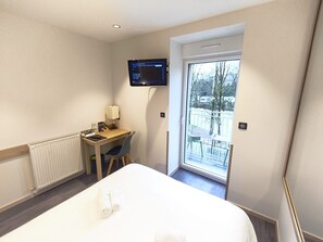 Et hotelværelse med seng, skrivebord med stol, fjernsyn og en balkon med udsigt.