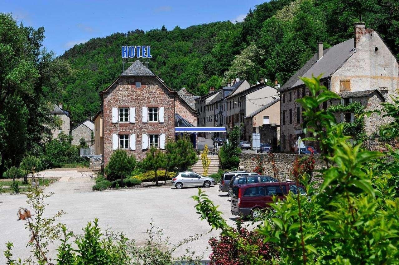 Ein Hotel mit einer Steinfassade, einem Parkplatz und einer Bergkulisse im Hintergrund.