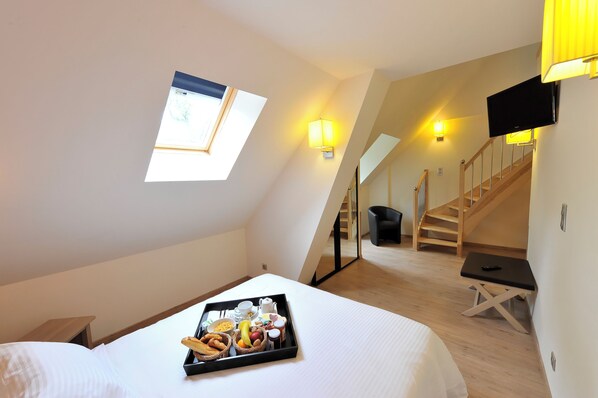 A hotel room with a bed, breakfast tray, skylight, staircase, and a TV mounted on the wall.