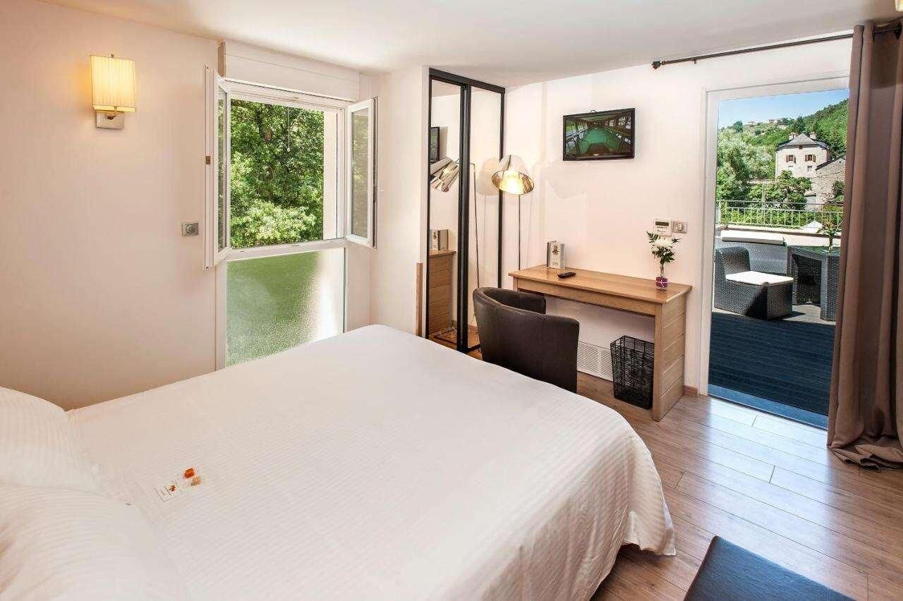 Une chambre d’hôtel comprenant un lit, un bureau, une chaise, un miroir, une télévision et un balcon avec des meubles d’extérieur.