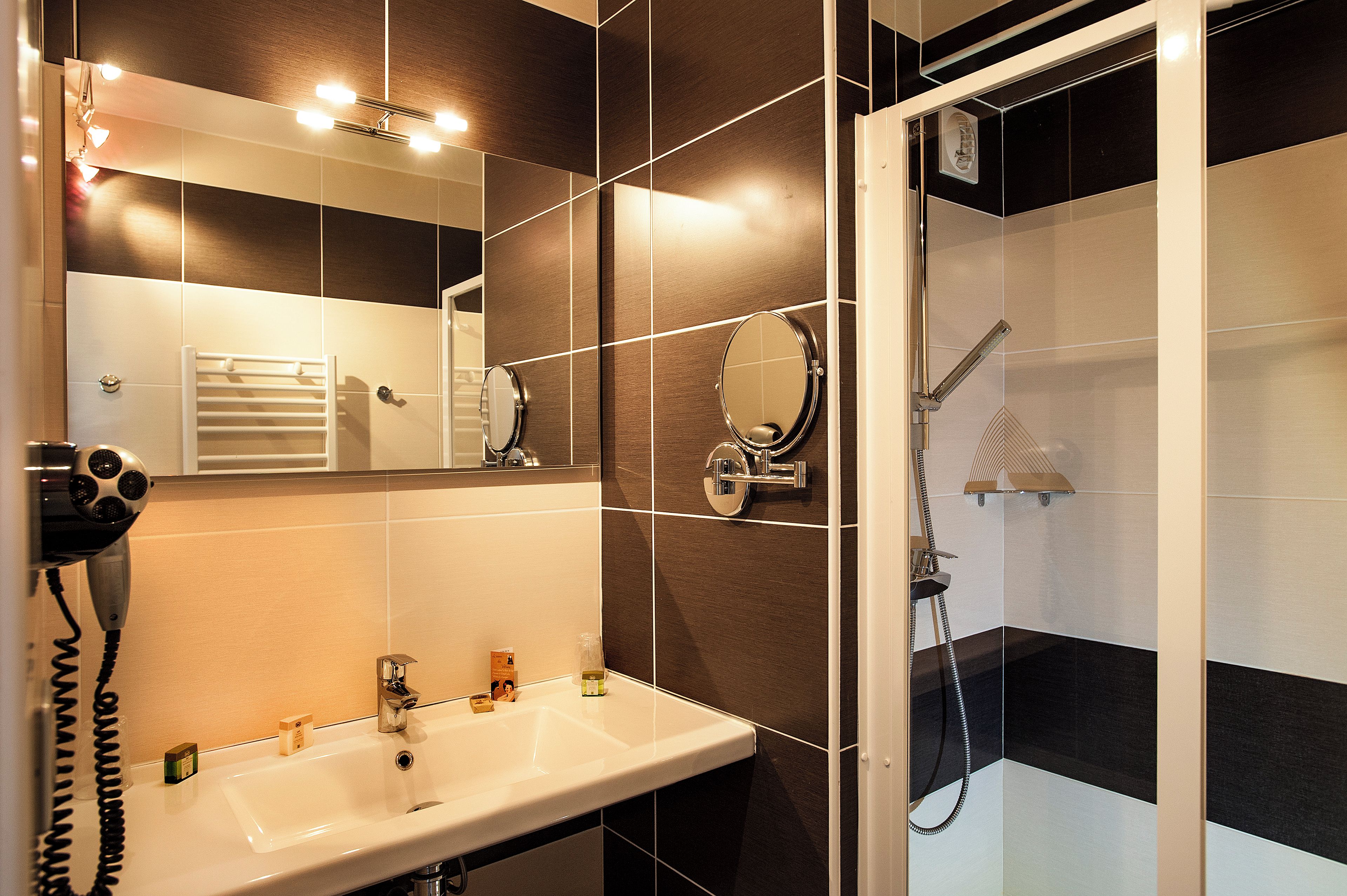 Une salle de bain avec un lavabo blanc, un miroir, un porte-serviettes et un espace douche.