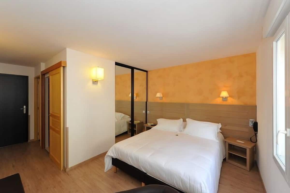 A hotel room with a bed, bedside tables, a mirror, and a window.