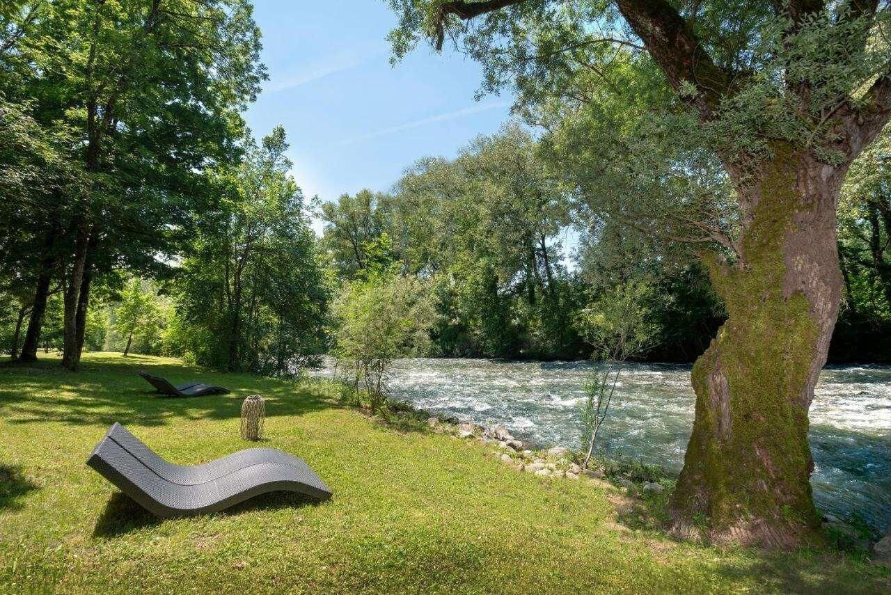 Uma área de relaxamento à beira do rio, com uma espreguiçadeira, uma mesa pequena e uma árvore.