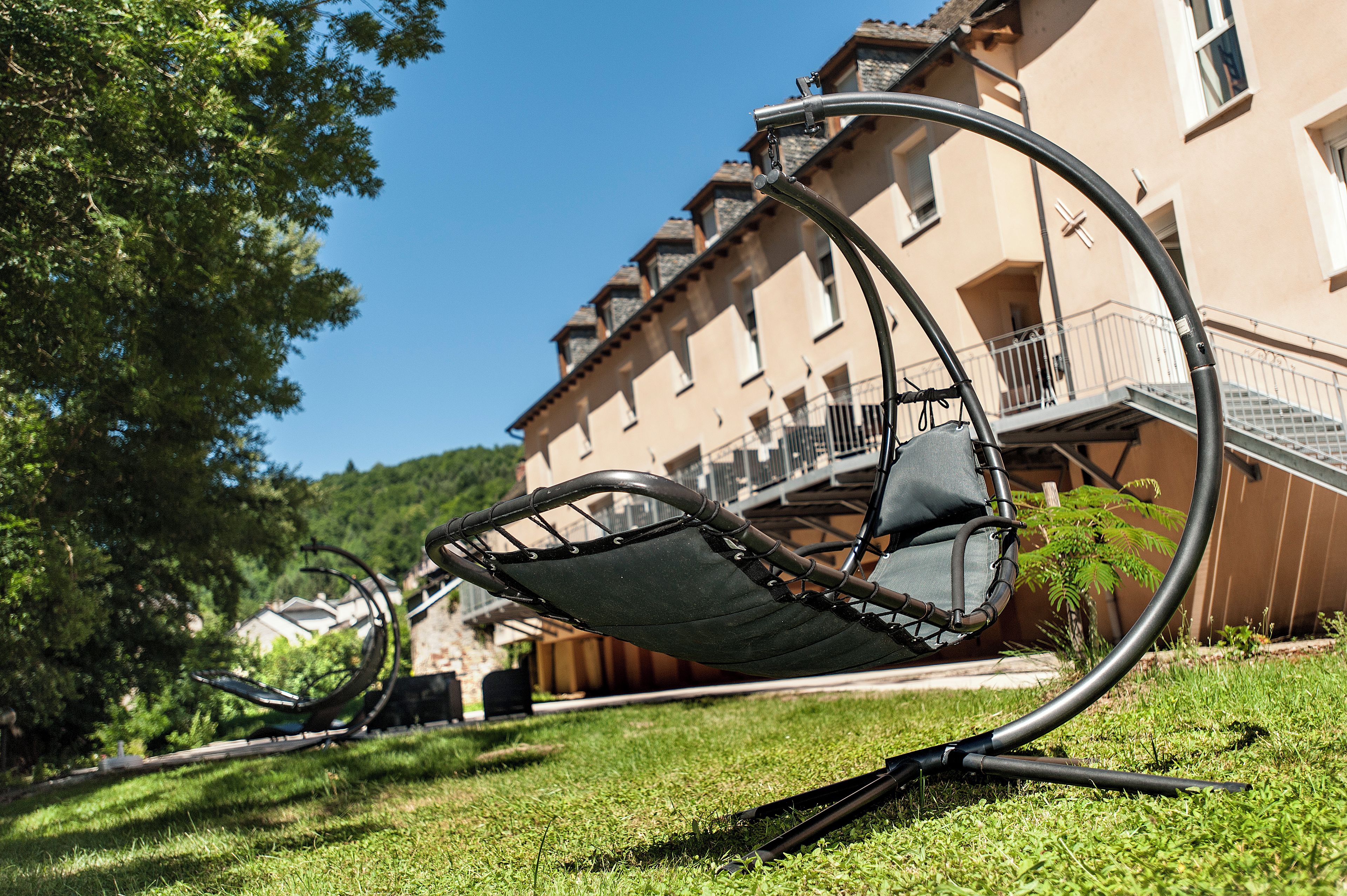 A garden chair with a metal frame and a cushion, positioned on grass in front of a building with a balcony.
