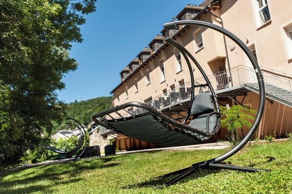 A garden chair with a metal frame and a cushion, positioned on grass in front of a building with a balcony.