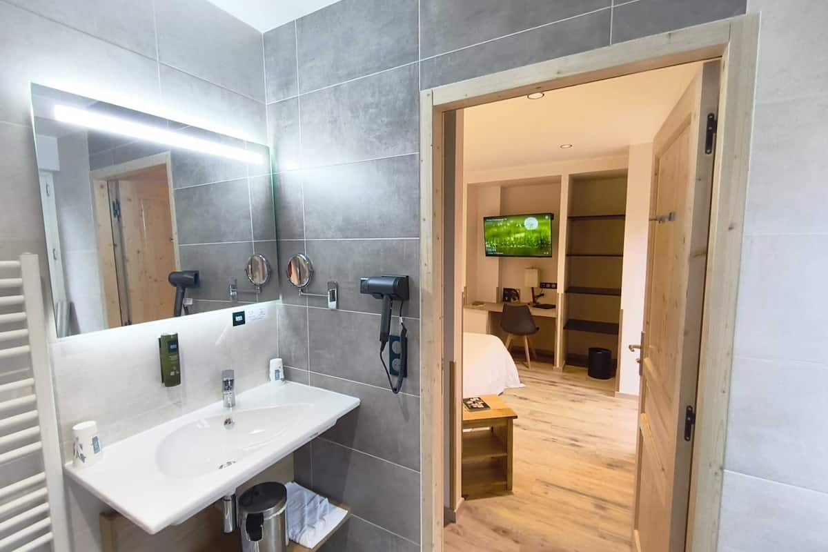 A modern bathroom with a large mirror, a sink, and a hairdryer. There is a television in the adjacent room.