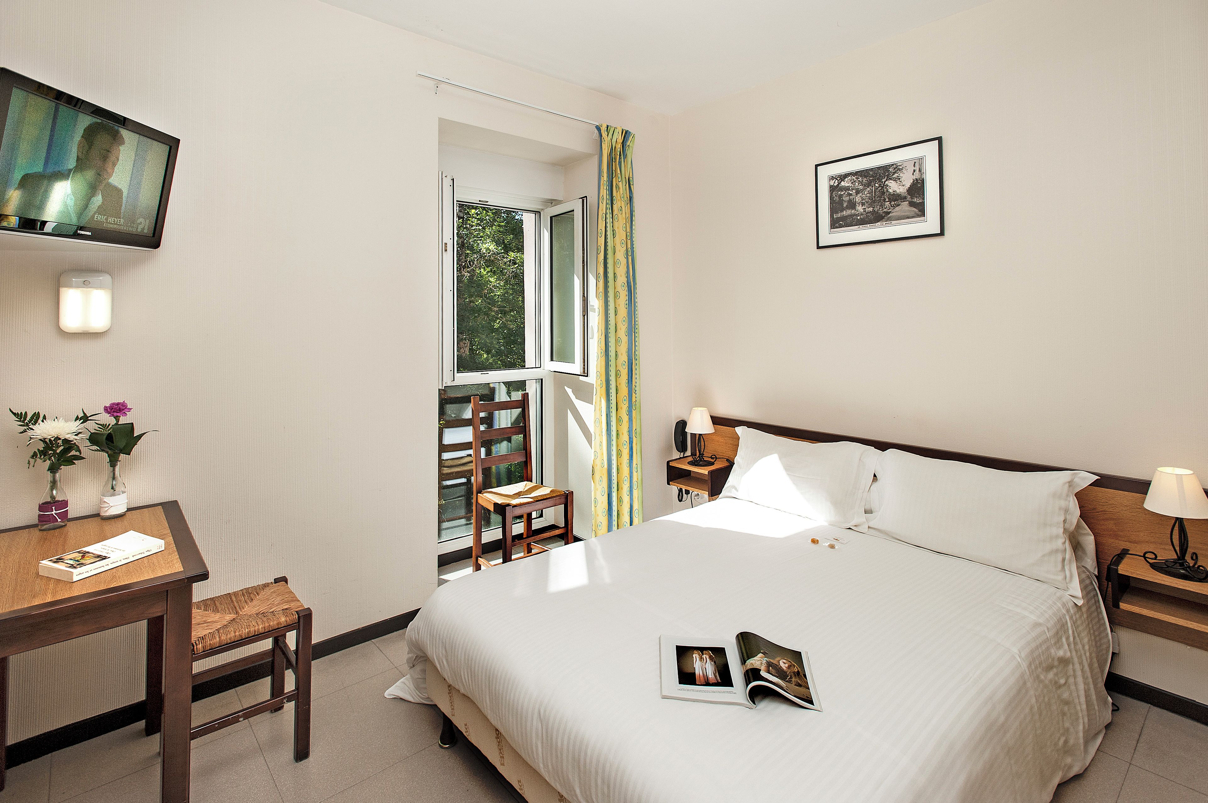 A hotel room with a bed, a desk, a chair, a television, a window, and a framed picture on the wall.