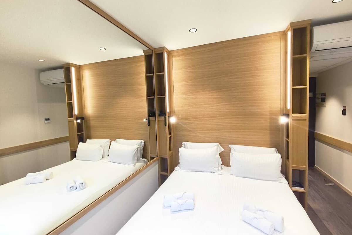 A hotel room with two beds, wooden paneling, and built-in shelving.