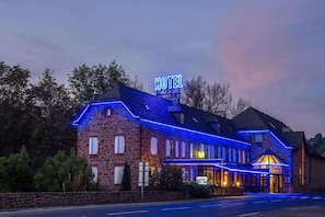 A hotel with a stone facade, a neon sign, and a classic architectural style.