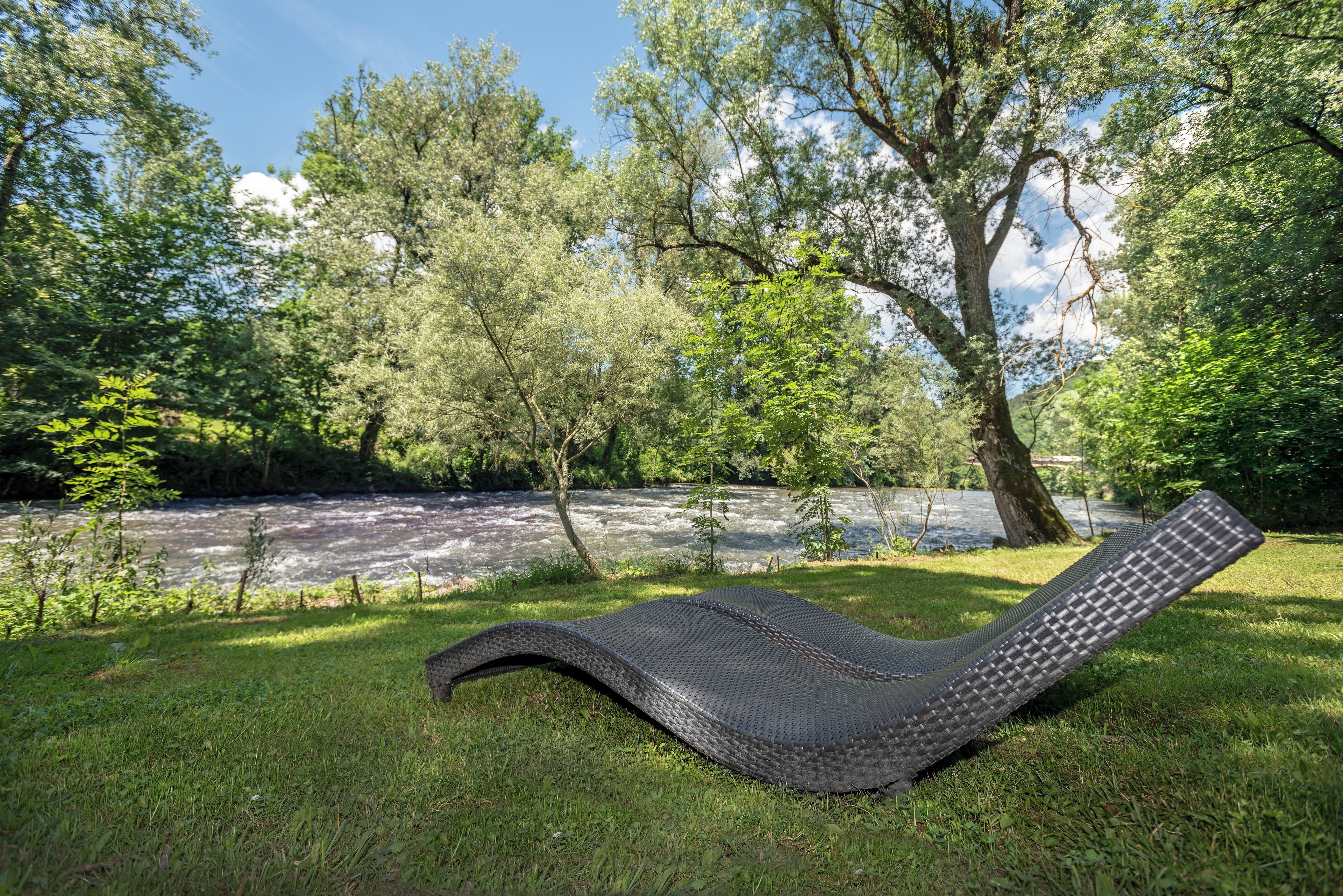 Un fauteuil inclinable posé sur l’herbe, près d’une rivière, entouré d’arbres.