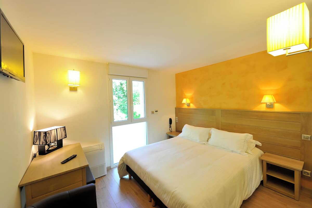 A hotel room with a bed, bedside tables, a desk with a lamp, and a window.