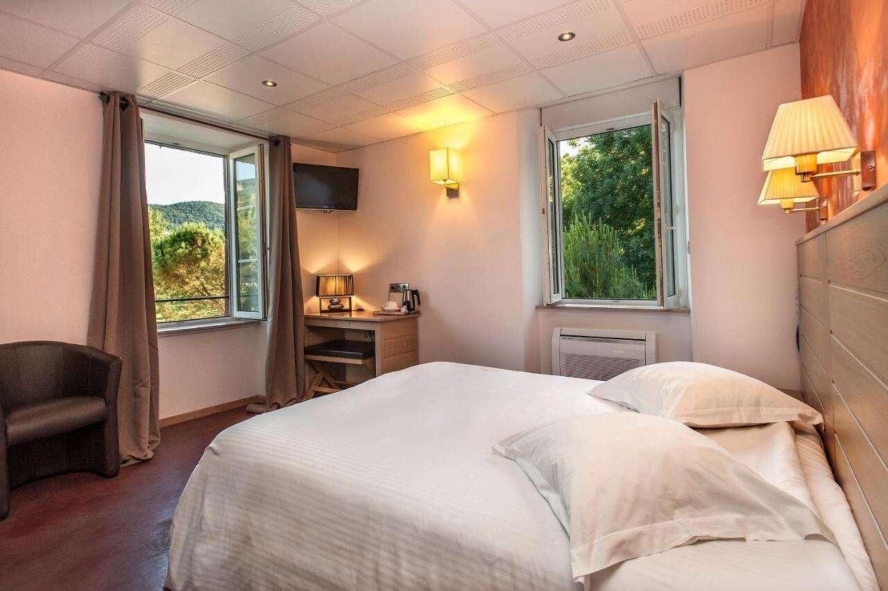 Una habitación de hotel con una cama, una silla, un escritorio con lámpara, un televisor y ventanas con cortinas.