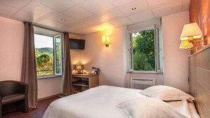Una habitación de hotel con una cama, una silla, un escritorio con lámpara, un televisor y ventanas con cortinas.