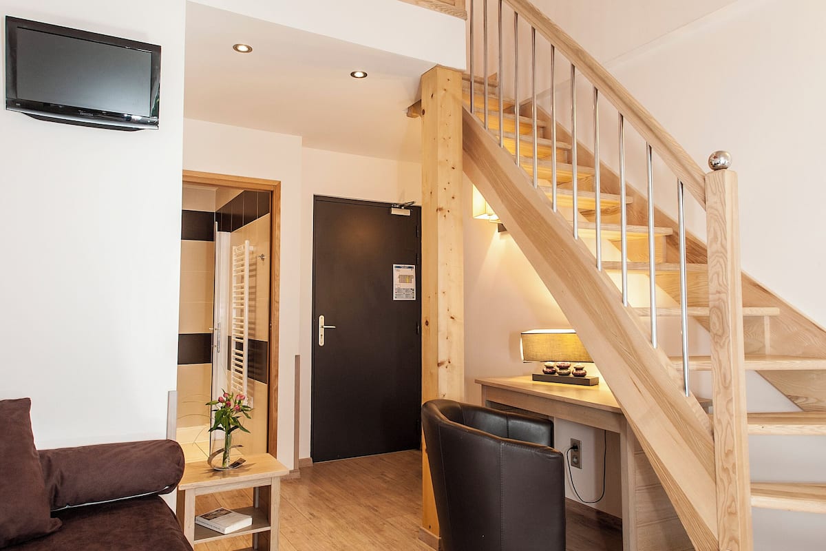 A spacious living area with a wooden staircase, a sofa, a coffee table, and a TV mounted on the wall.