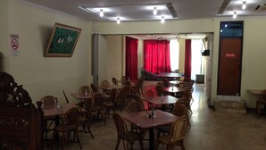 A dining area with tables and chairs, a piano, and a door with a sign. - Hotel Lautze Indah (Jakarta)