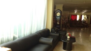 A spacious lobby with a black leather sofa, a round coffee table with a vase, and a large grandfather clock. - Hotel Lautze Indah (Jakarta)
