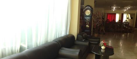 A spacious lobby with a black leather sofa, a round coffee table with a vase, and a large grandfather clock.