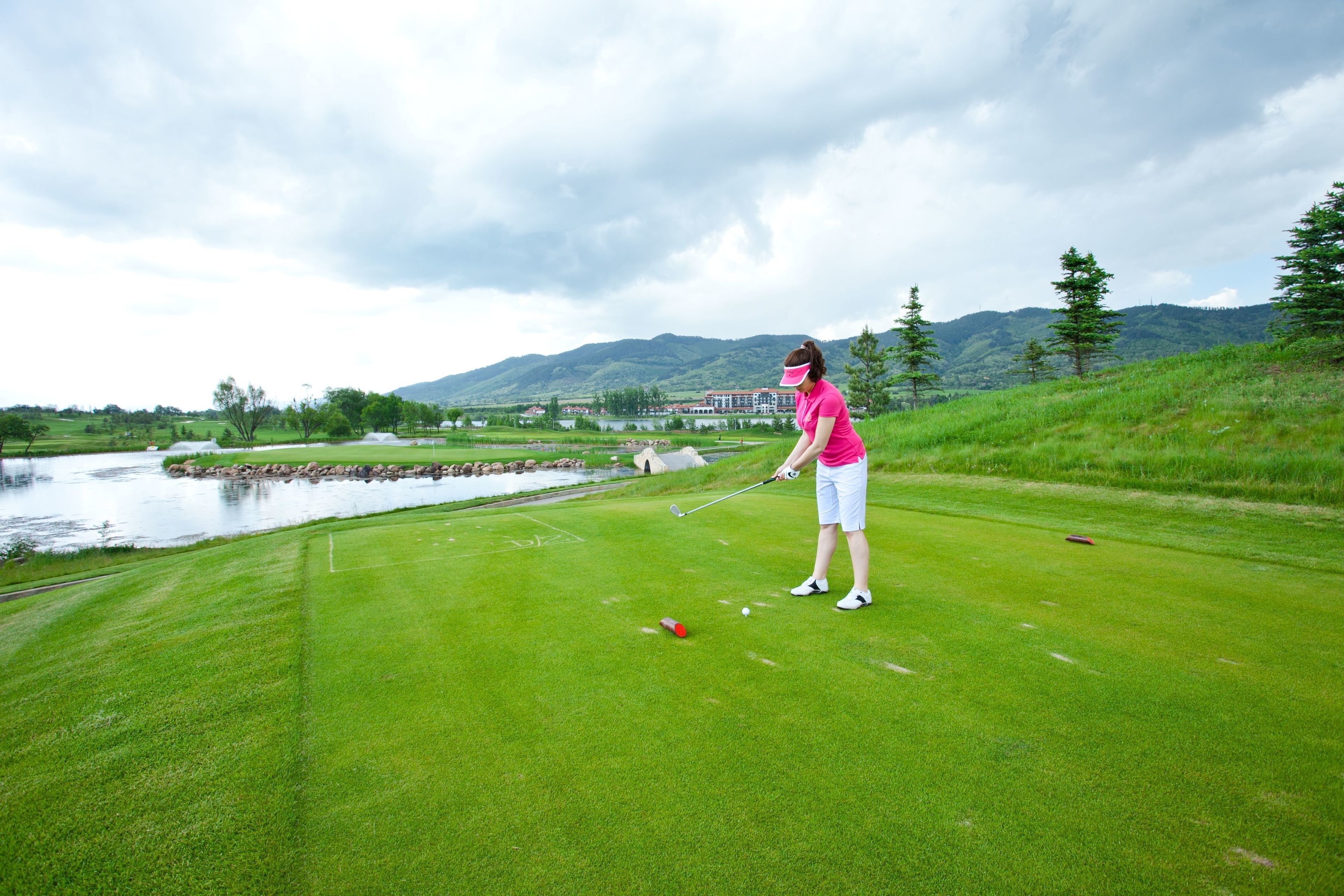 Un campo de golf con un estanque, árboles y un edificio al fondo.