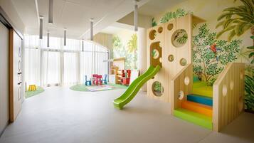 Zona de juegos para niños con un tobogán, escaleras de colores y un mural con motivo de una selva.