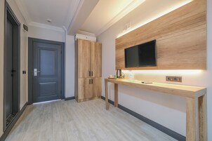 Un pasillo con una puerta oscura, armarios de madera, un escritorio de madera y un televisor de pantalla plana, además de un panel de pared iluminado.