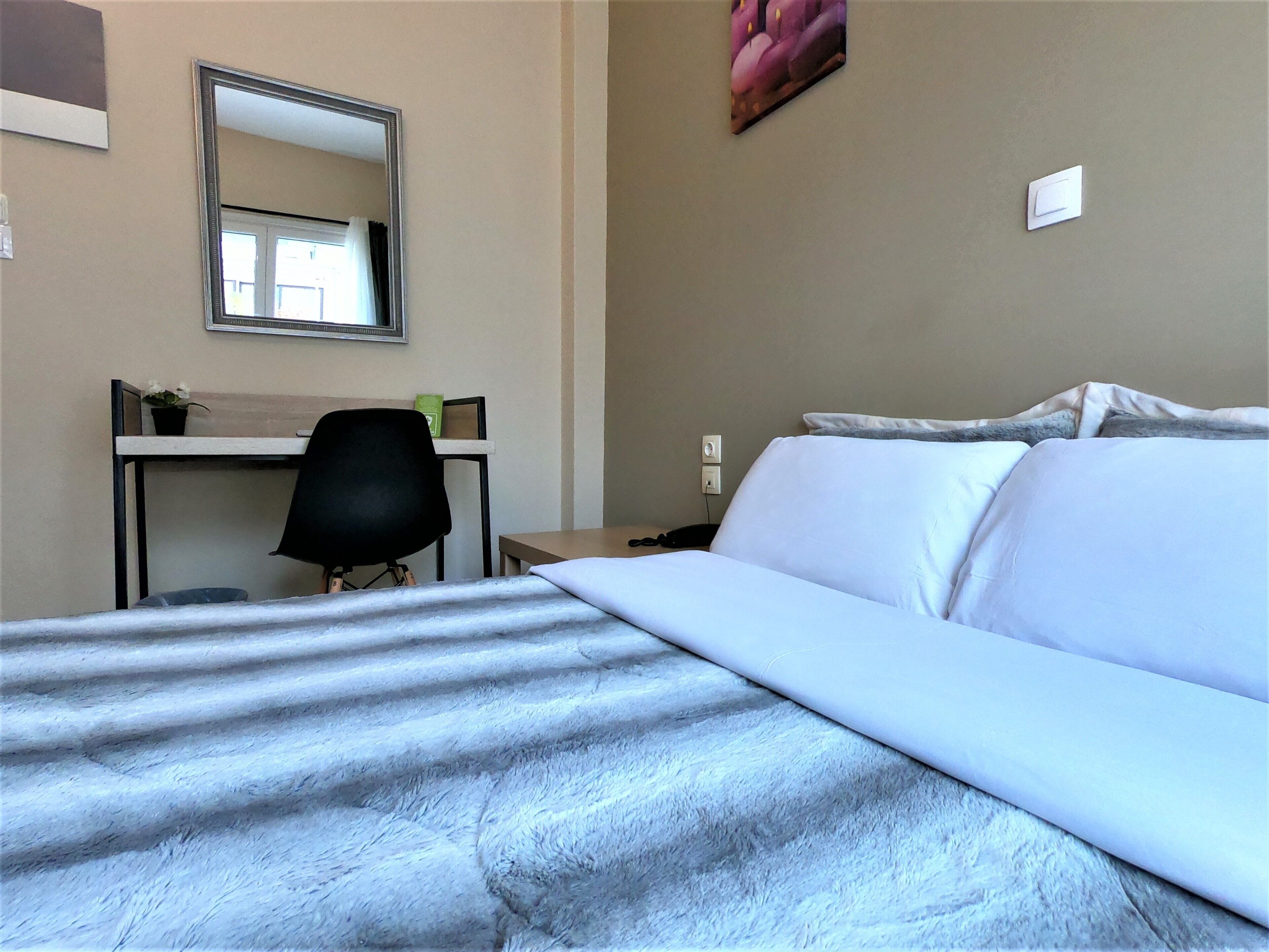 Habitación de hotel con cama, escritorio, silla, espejo e interruptor de luz en la pared.