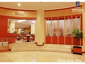 Un hall d’hôtel comprenant un comptoir d’accueil, un café appelé « Selera Coffee Shop » et un escalier menant à l’étage supérieur.