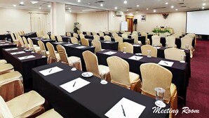 Uma sala de reuniões com mesas e cadeiras dispostas em fileiras, uma tela de projetor e um quadro branco.
