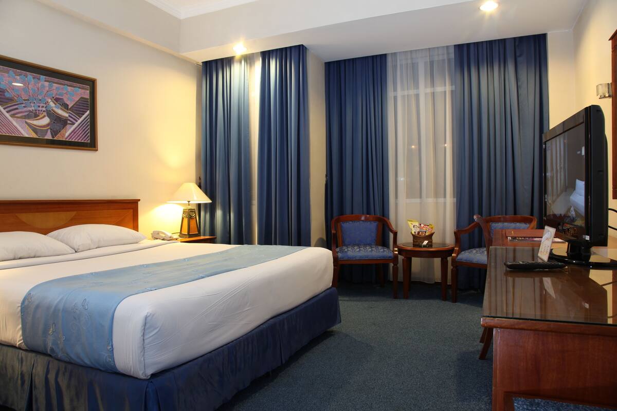Una habitación de hotel con una cama grande, dos sillones, un escritorio, un televisor y un cuadro en la pared.