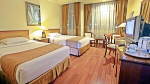 Quarto de hotel com duas camas, uma escrivaninha com computador, televisão e mesa de jantar com cadeiras.