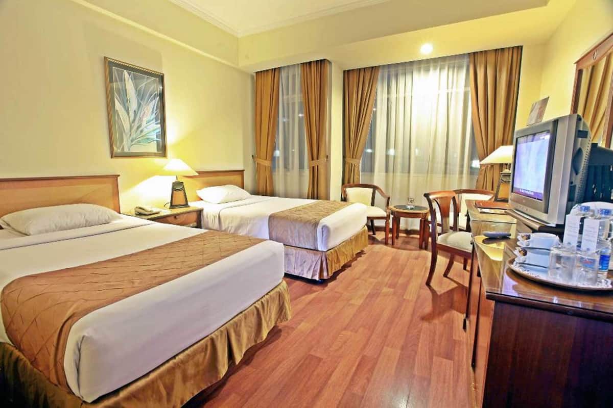Habitación de hotel con dos camas, un escritorio con computadora, televisión y una mesa de comedor con sillas.