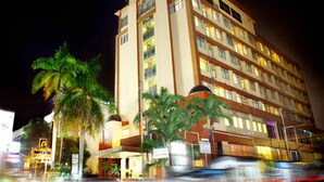 Hotel de vários andares com design moderno, destacando uma entrada imponente com área coberta e diversas palmeiras na frente.