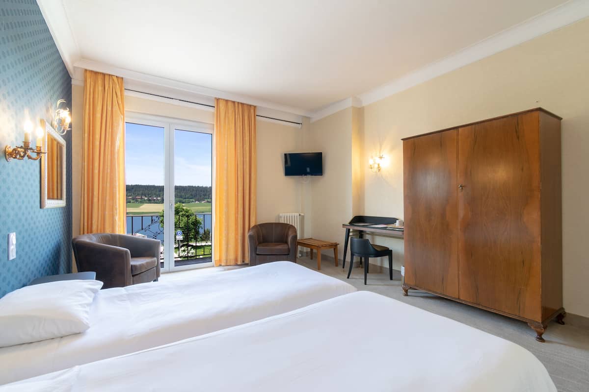 A hotel room with a large bed, a desk, two chairs, a wardrobe, and a TV.
