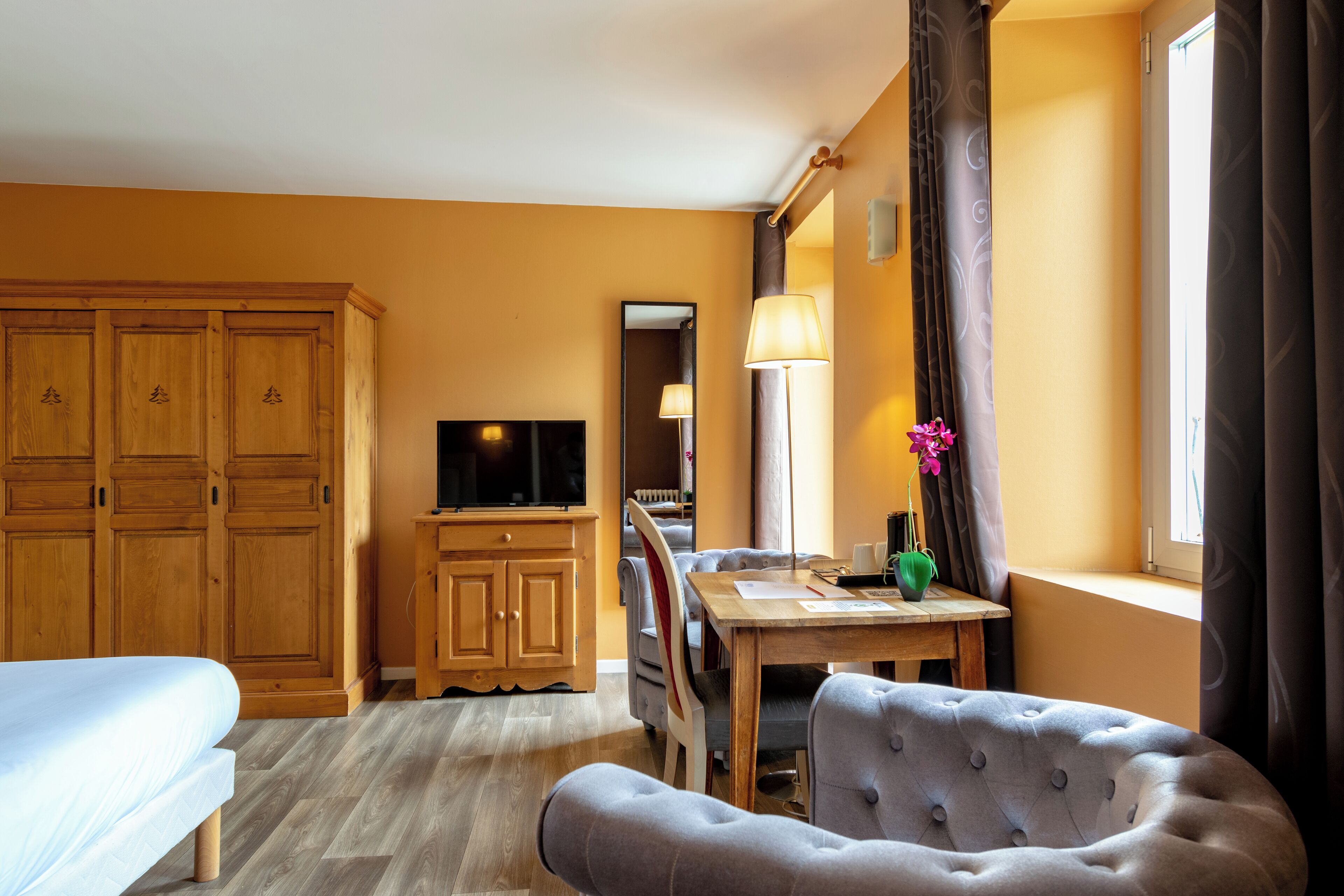 Una camera d'albergo con un letto, una televisione, una scrivania con lampada, una sedia e un armadio.