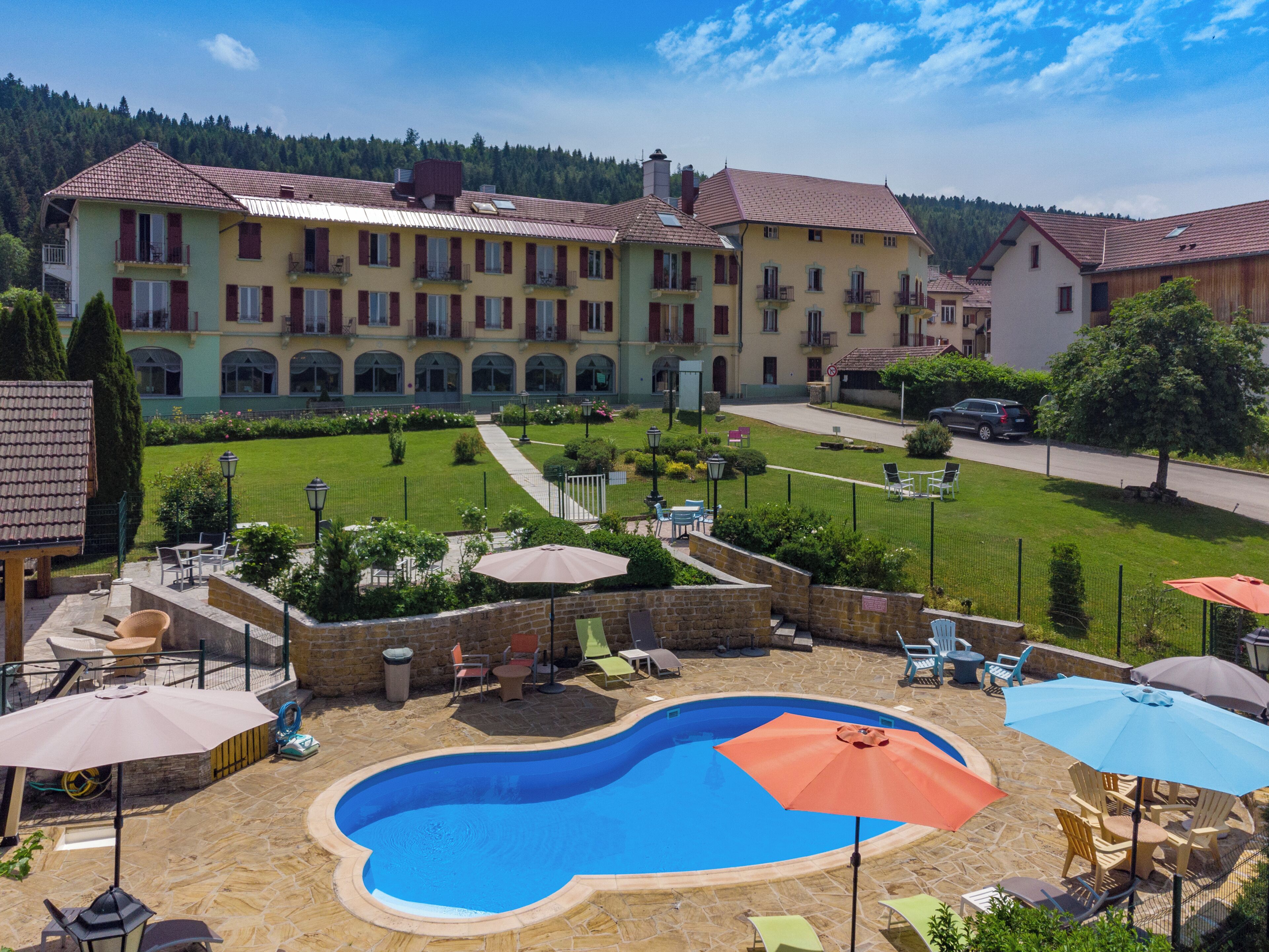 A hotel with a swimming pool, outdoor seating, and a view of the surrounding landscape.
