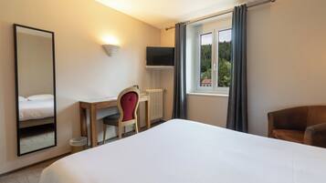 A hotel room with a large bed, a desk with a chair, a television mounted on the wall, and a window with curtains.