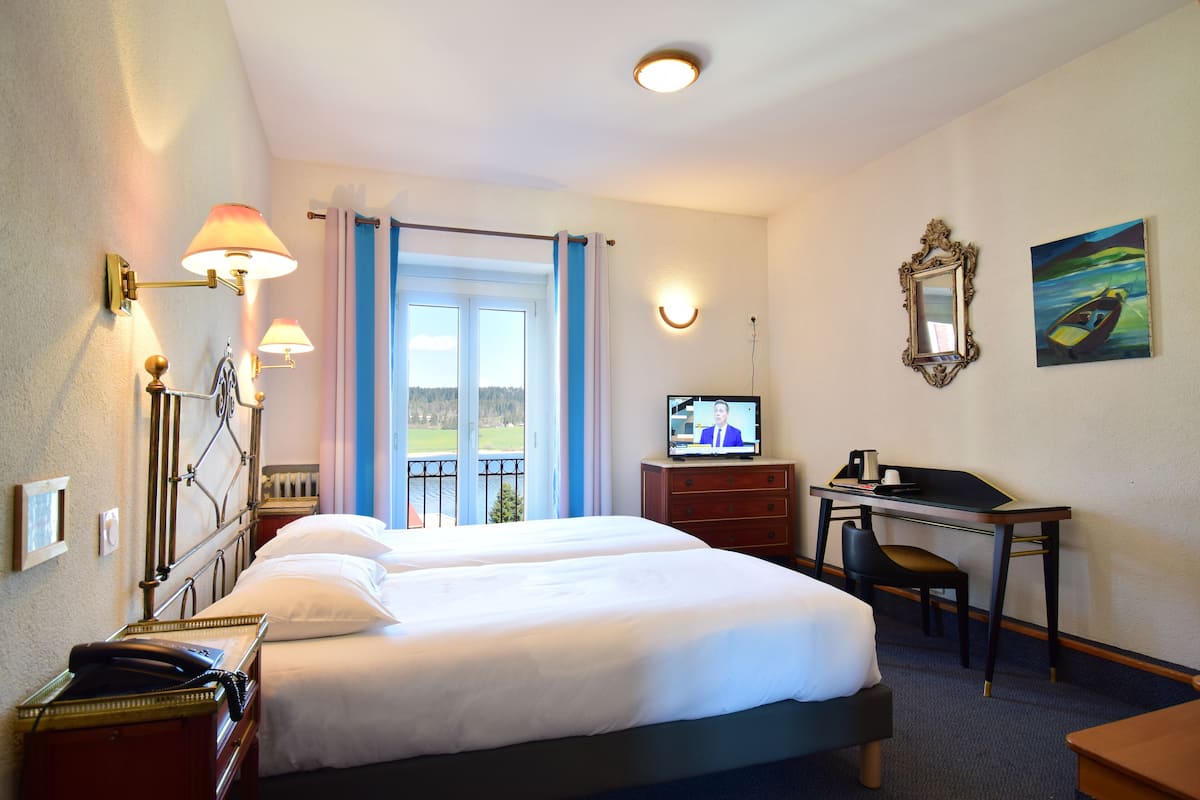 A hotel room with two beds, a desk, a television, and a balcony with a view of the outdoors.