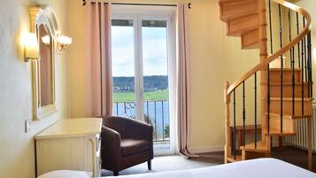 A bedroom with a bed, a chair, a desk, a mirror, a window with curtains, and a wooden staircase.